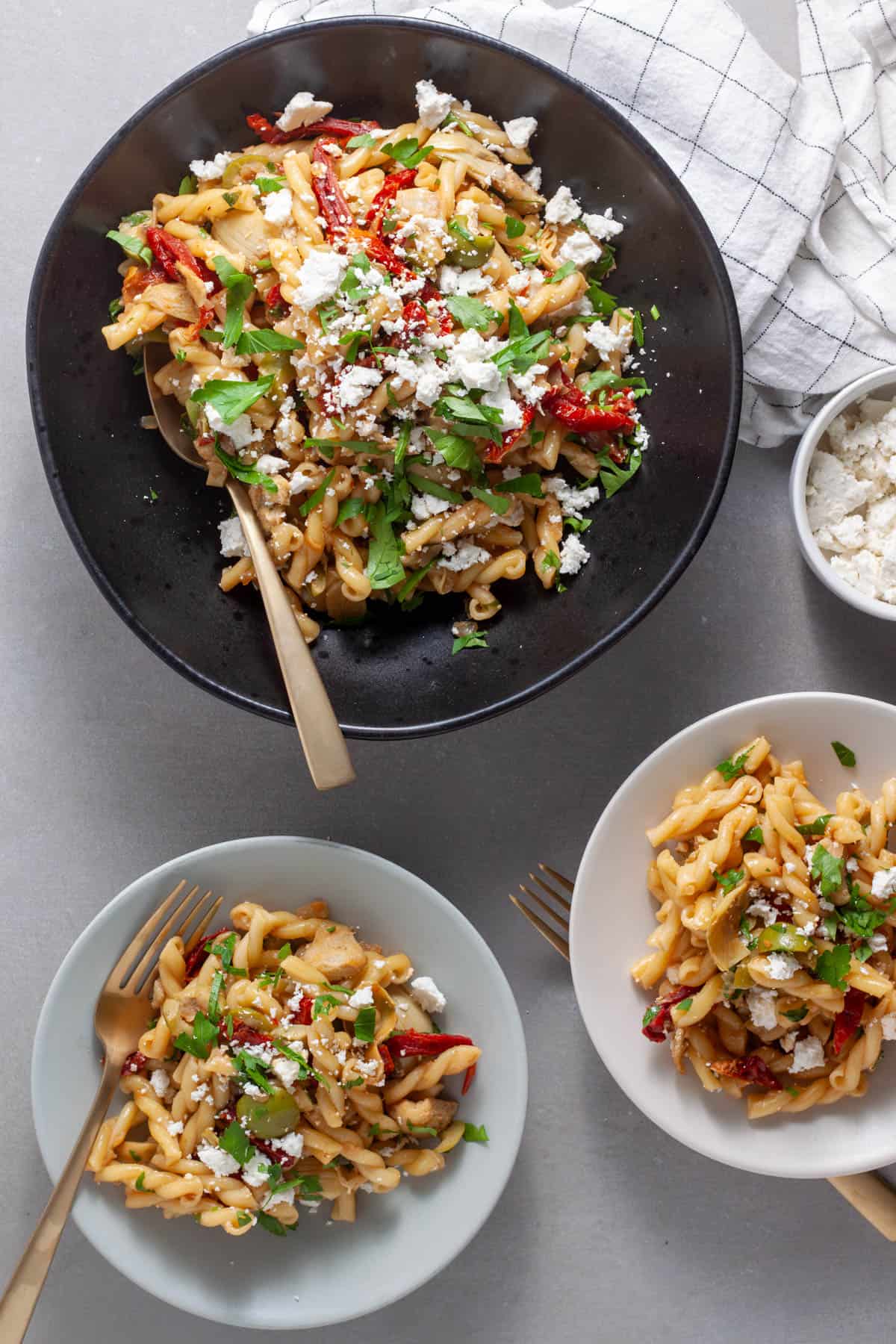 Sun-dried tomato and artichoke pasta in a large serving bowl with servings in a smaller plates.
