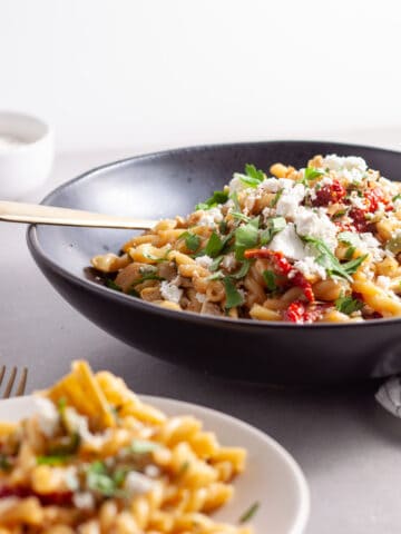 Sun-dried tomato and artichoke pasta in a black serving bowl topped with ricotta salata and parsley.