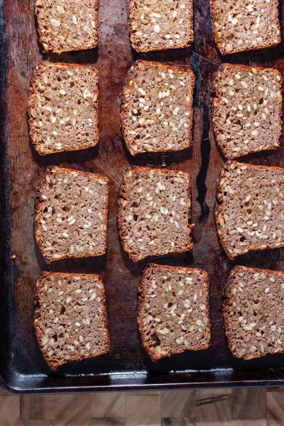 Pumpernickel bread cut into thin slices and brushed with caper oil on a baking sheet.