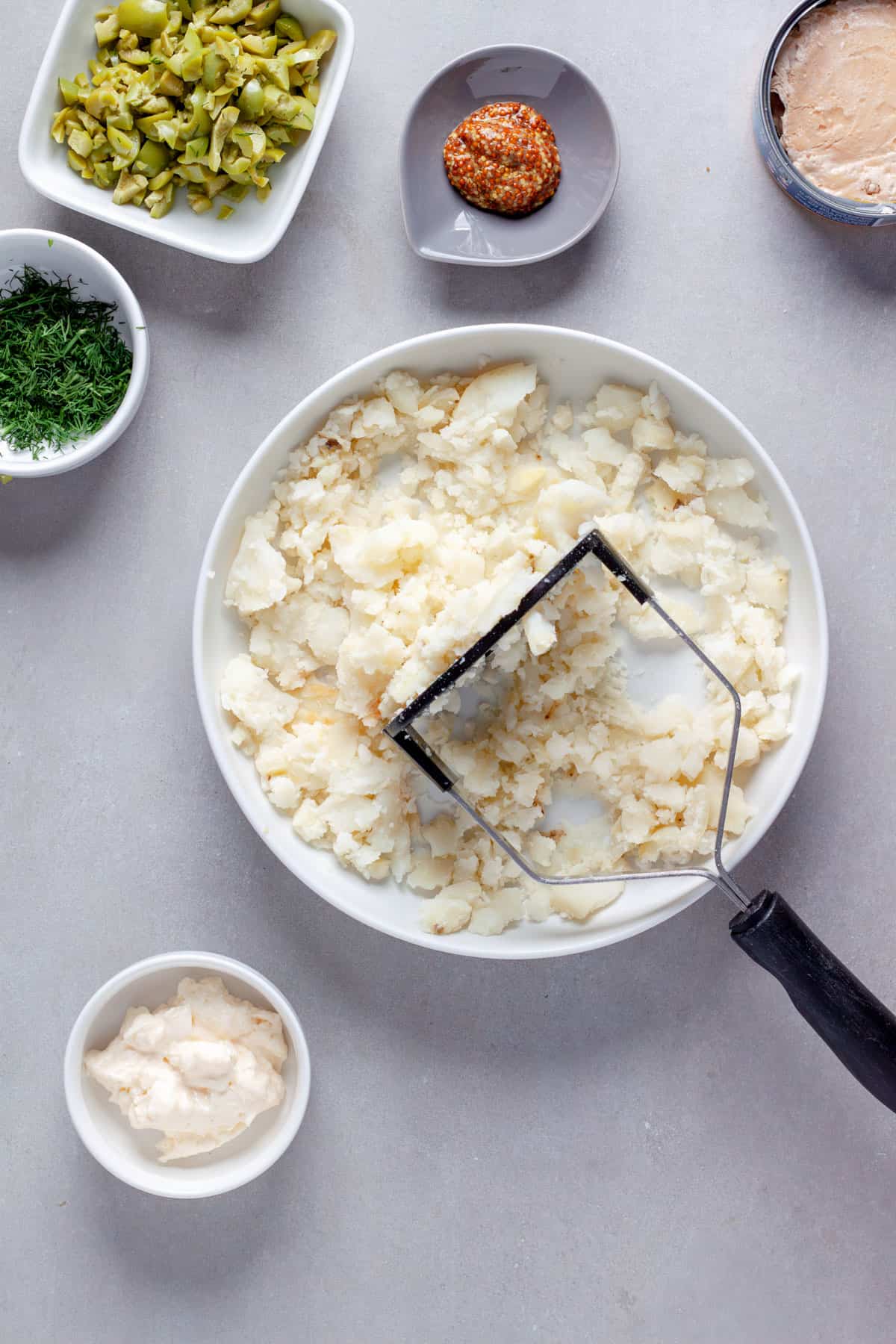 A potato in a bowl getting mashed for tuna croquettes.