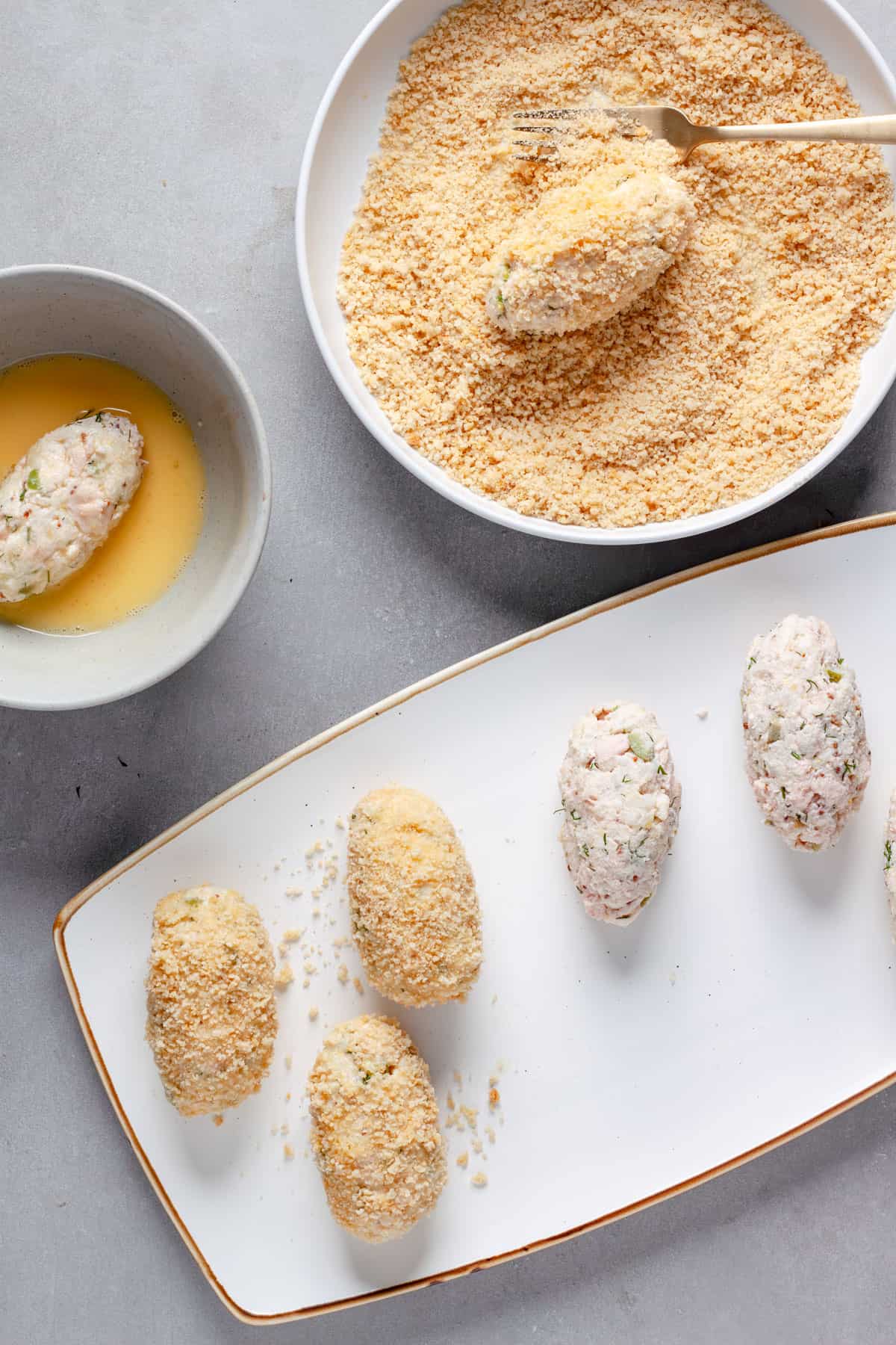 Uncooked tuna croquettes in a plate getting dipped in egg and panko.