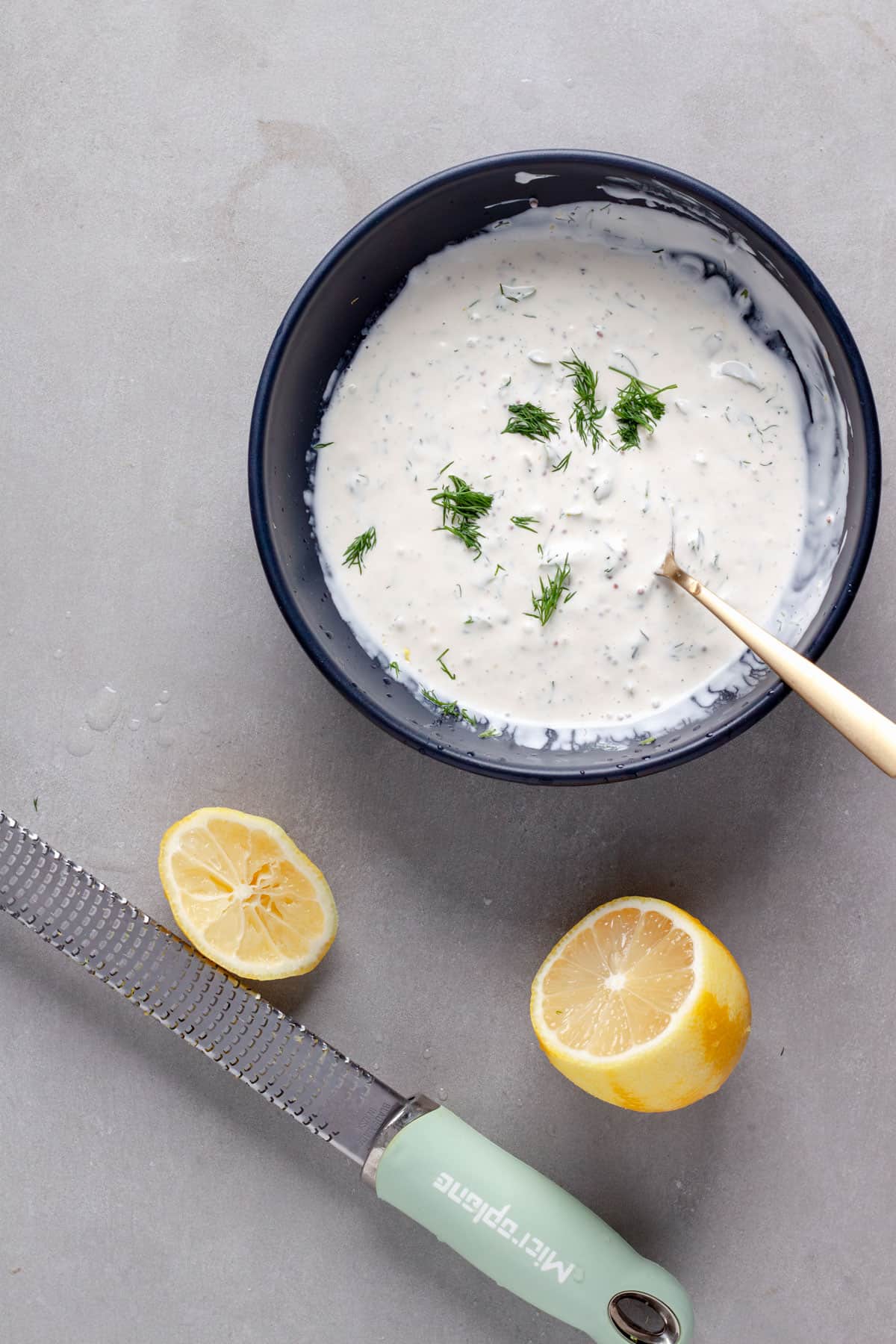 A homemade tartar sauce in a bowl with a lemon and microplane to the side.
