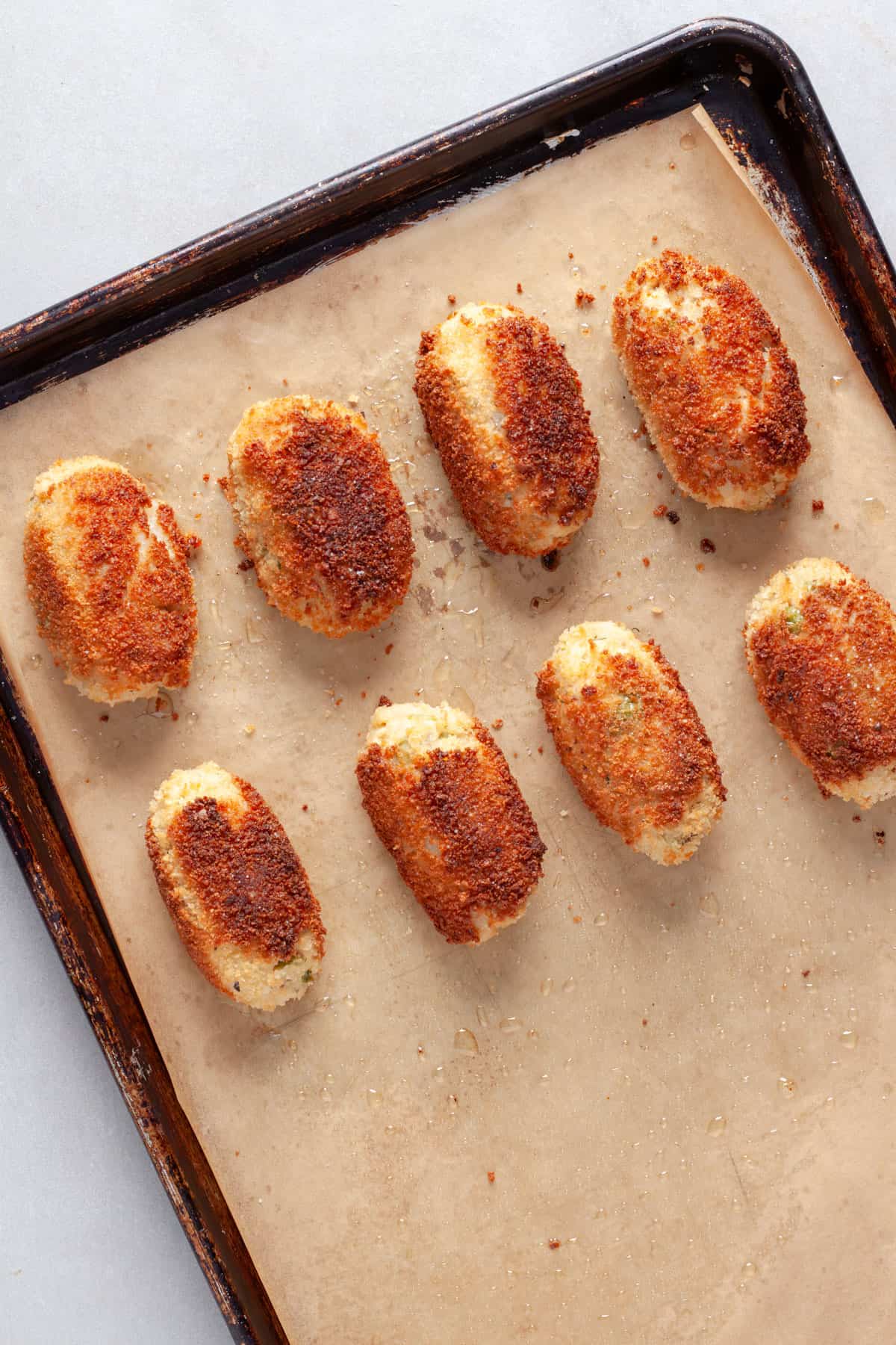 Crispy tuna croquettes on a parchment lined baking sheet.