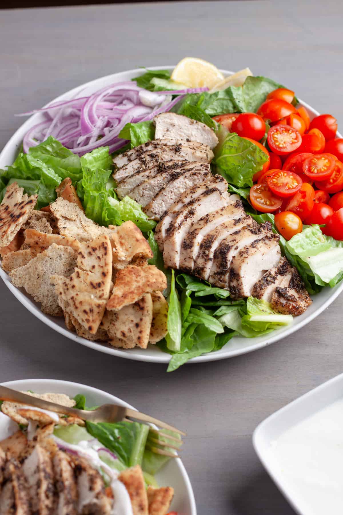 A platter of za'atar chicken with crispy pita salad and a lemon yogurt sauce to the side.