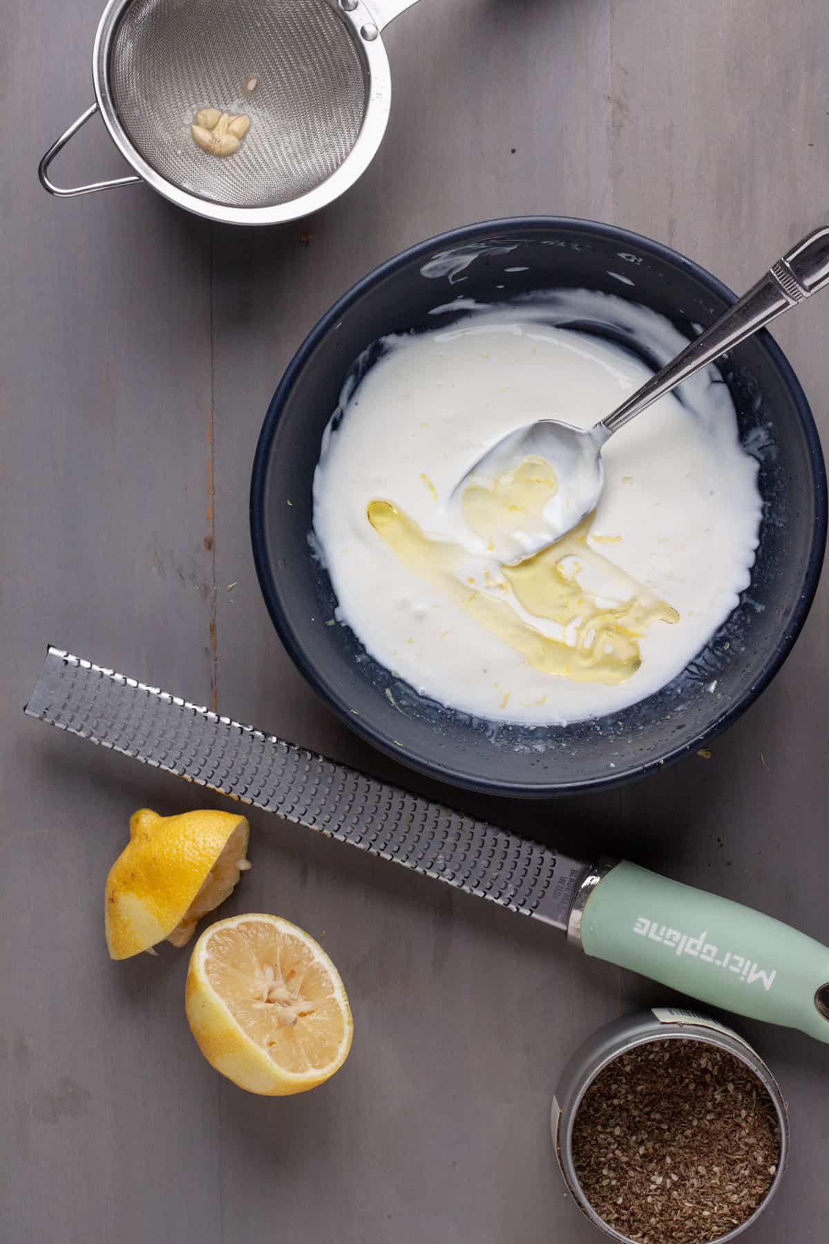 A lemon yogurt dressing in a blue bowl with a micrplane to the side with a lemon cut in half.