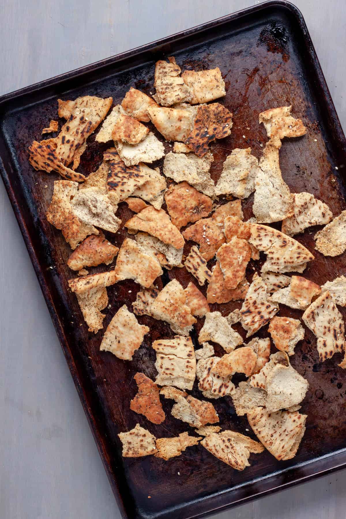 Torn pieces of pita on a baking sheet drizzled with oil and sprinkled with za'atar seasoning.