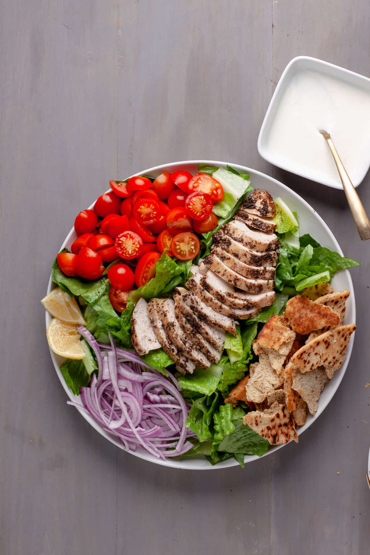 A platter of za'atar chicken with crispy pita salad and a lemon yogurt sauce to the side.