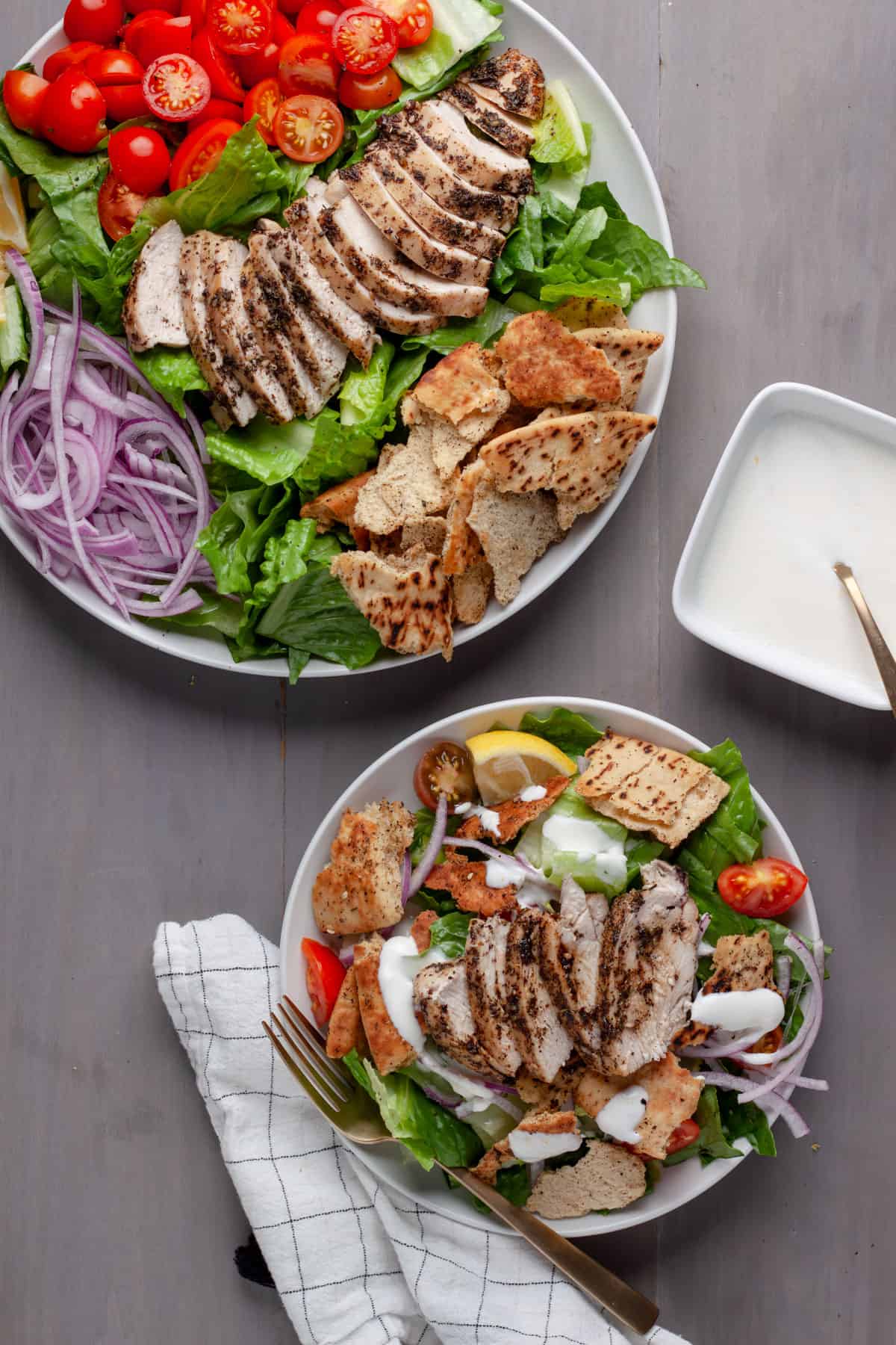 A platter of za'atar chicken and crispy pita salad with a serving on a small plate and lemon yogurt sauce to the side.