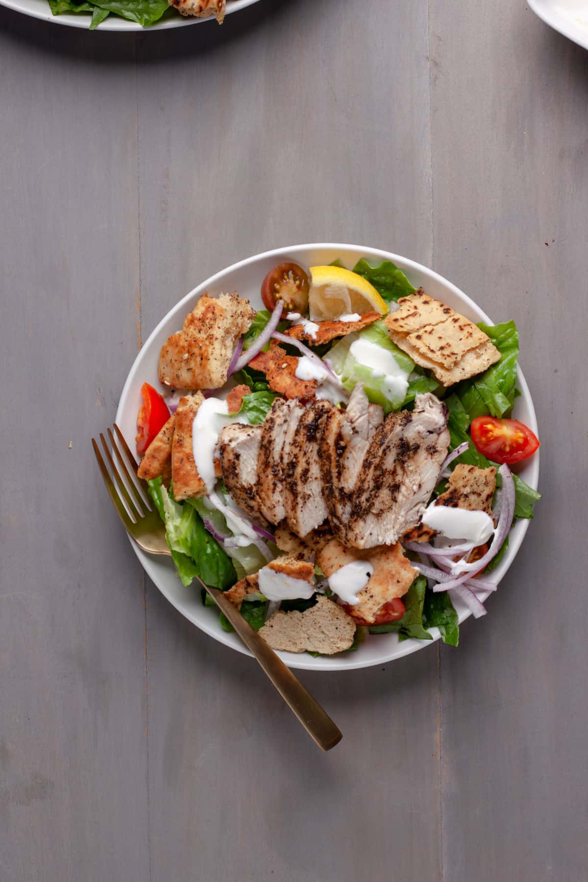 A serving of a za'atar chicken and crispy pita salad in a bowl topped with a lemon yogurt sauce.