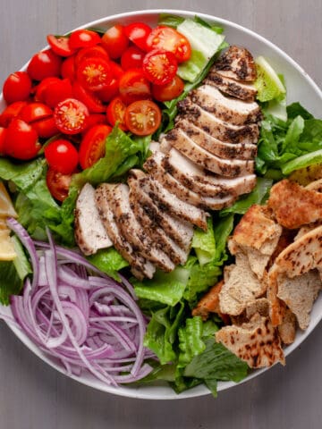 A platter of za'atar chicken with crispy pita salad and a lemon yogurt sauce to the side.