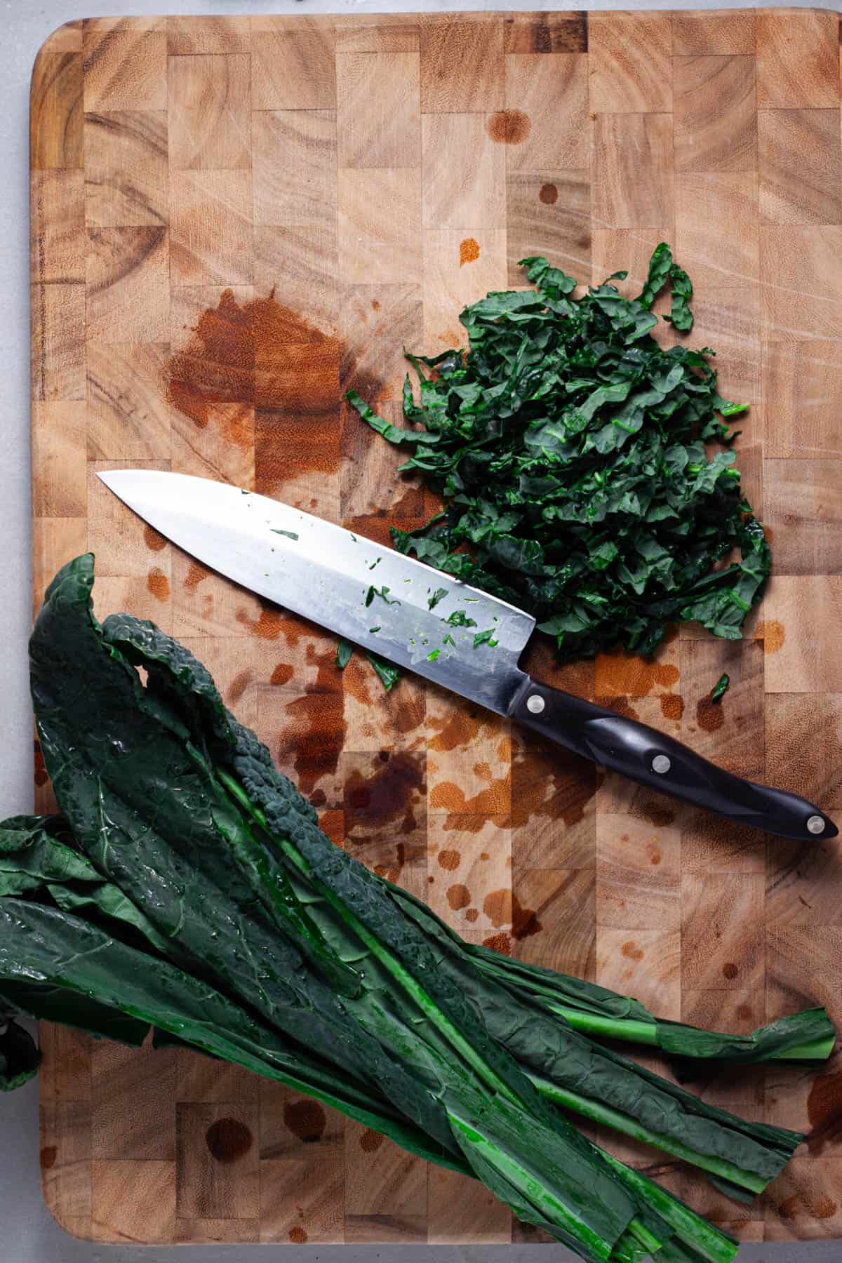 Kale getting chopped on a wooden cutting board.