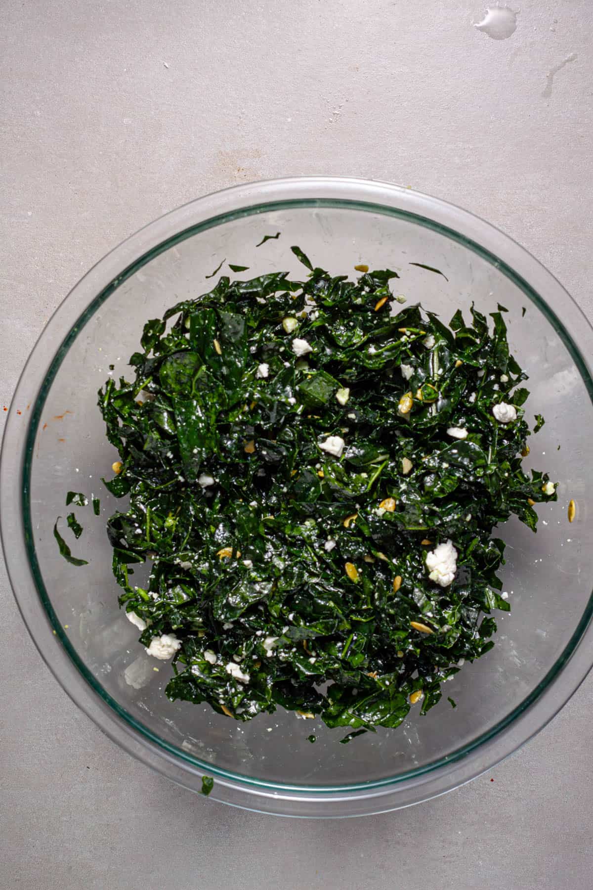 A bowl of kale massaged with oil and lemon and feta and pepitas added.