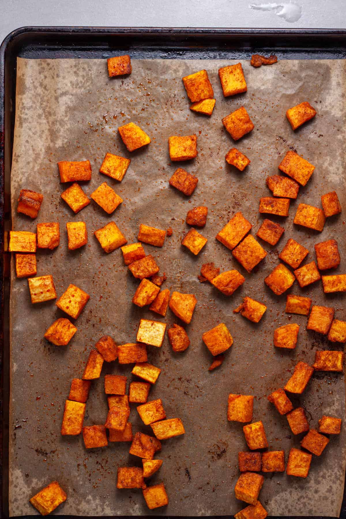 Butternut squash cubes roasted on a parchment lined baking sheet.