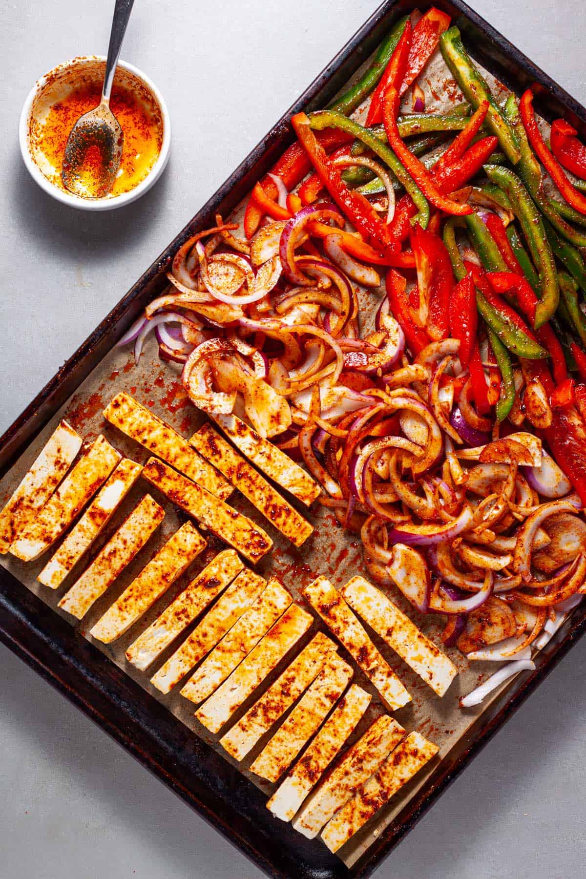 A sheet pan with sliced peppers and onions and firm tofu getting ready to be roasted for tofu fajitas.