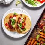 Sheet pan tofu fajita on a gray table with a small plate serving topped with cilantro, tomatoes and avocado.