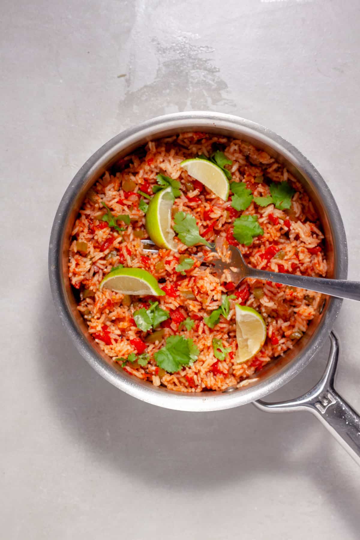 Tomato rice in a medium saucepan topped with fresh cilantro and lime wedges.