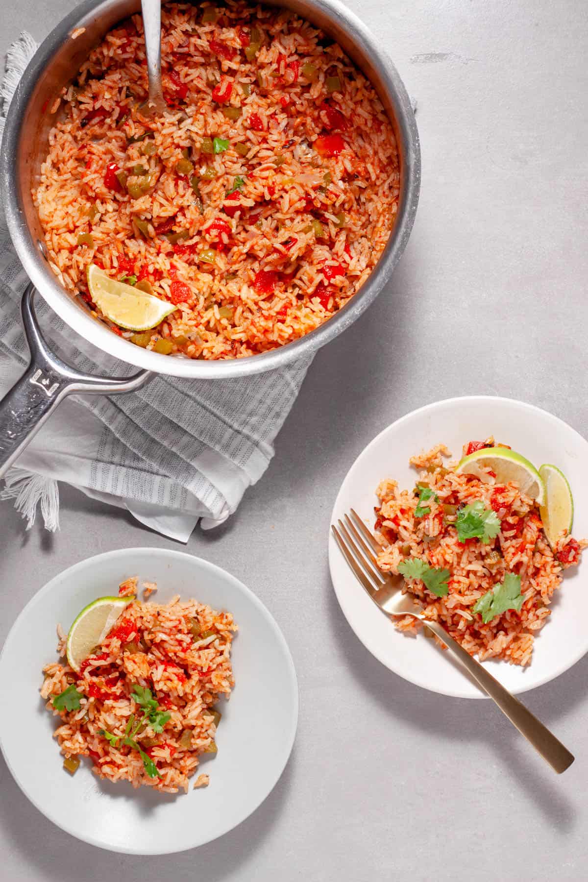 A couple servings of tomato rice on small plates with a saucepan of more rice to the side.