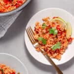 A plate of tomato rice (Mexican Rice) topped with fresh cilantro and lime wedges.
