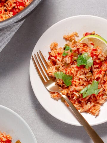 A plate of tomato rice (Mexican Rice) topped with fresh cilantro and lime wedges.