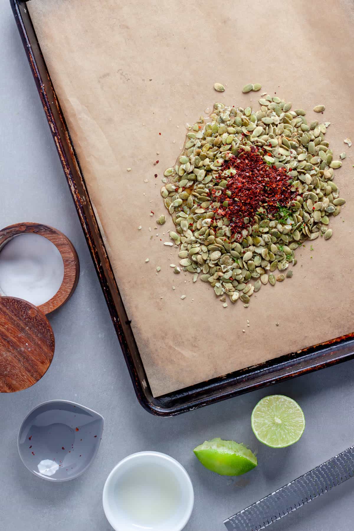 A sheet tray with pepitas, chili powder and lime zest getting ready to get baked for chili lime pepitas.