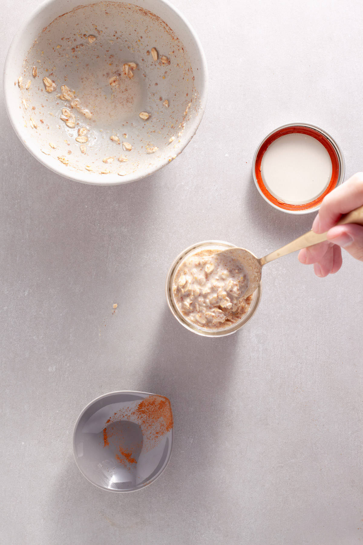 A spoon adding cinnamon overnight oats to a mason jar.