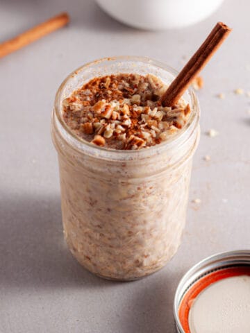 A small mason jar with cinnamon overnight oats topped with cinnamon and chopped pecans.