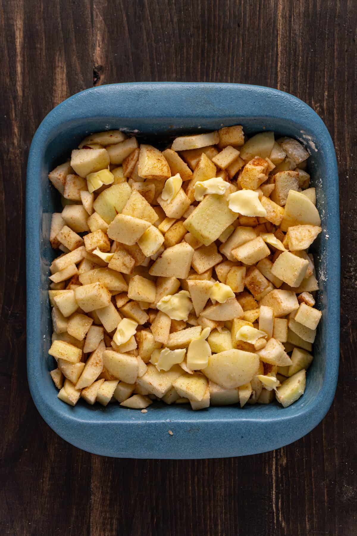 Chopped apples tossed with a bit of gluten-free apples and cinnamon in a baking dish.