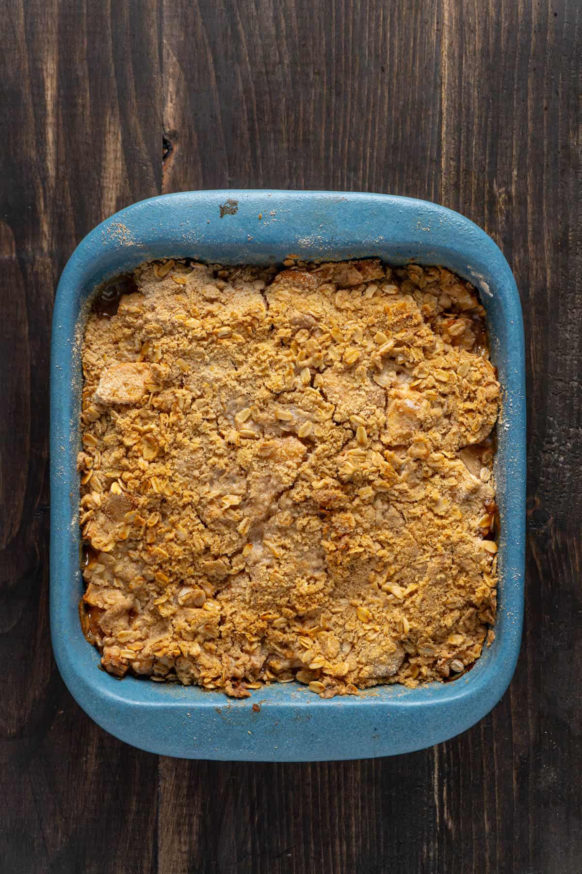 A baked gluten-free apple crisp in a blue baking dish on a dark table.