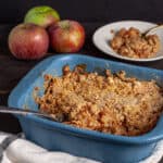 A blue baking dish with gluten-free apple crisp and apples in the background.