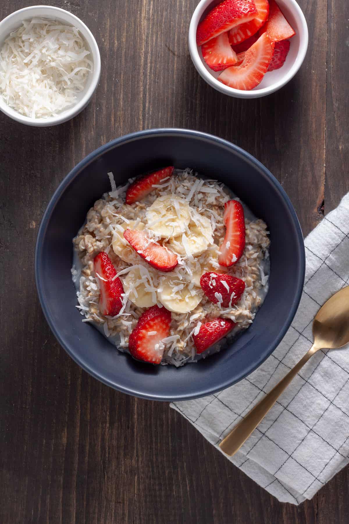 A serving of coconut overnight oats in a blue bowl topped with strawberries, shredded coconut and bananas.