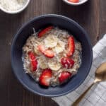 A bowl of overnight oats with coconut milk topped with shredded coconut, berries and maple syrup.