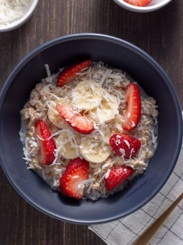 A bowl of overnight oats with coconut milk topped with shredded coconut, berries and maple syrup.