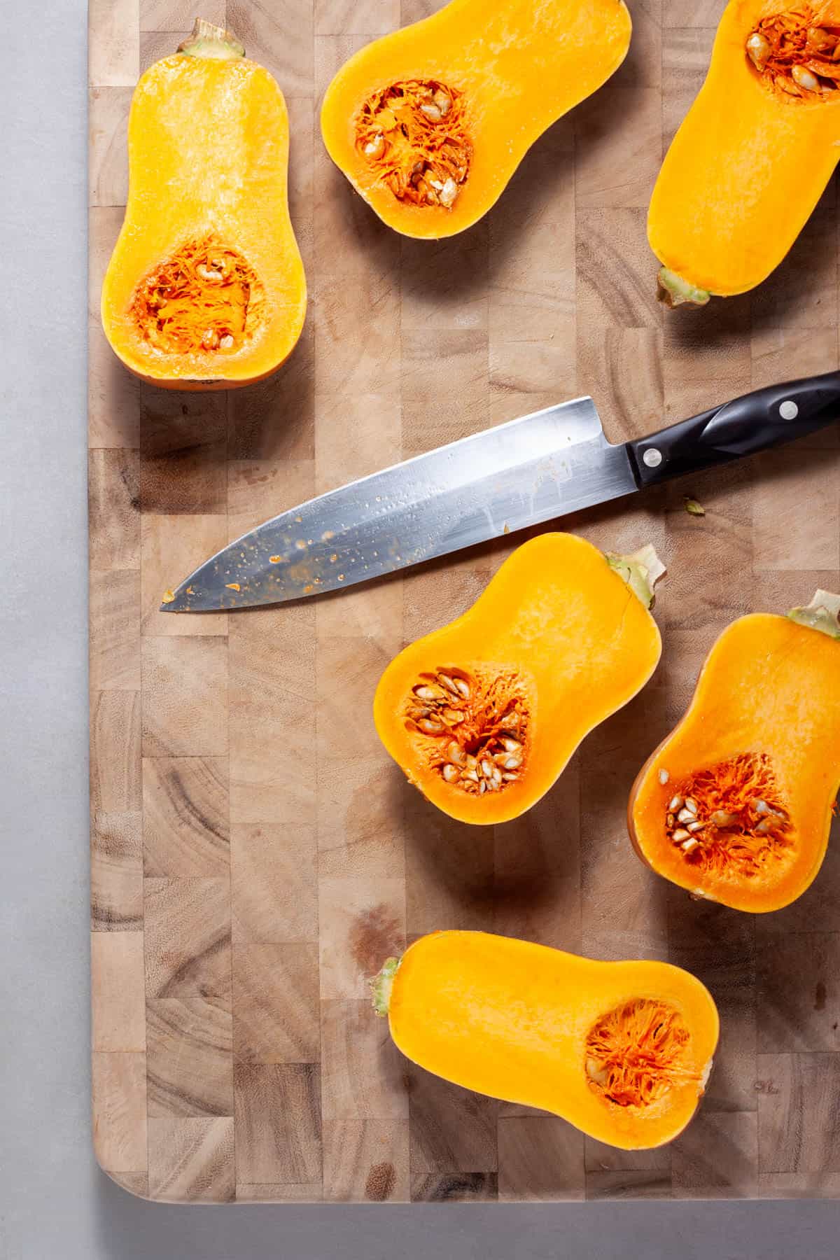 Honeynut squash getting cut in half on a wooden cutting board.