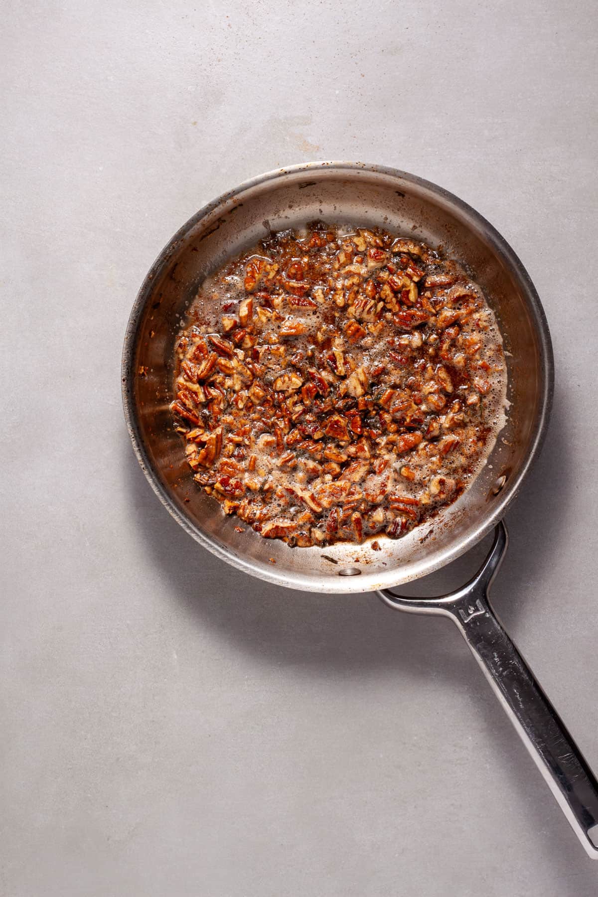 Toasted pecans with maple syrup and sage in a small skillet.