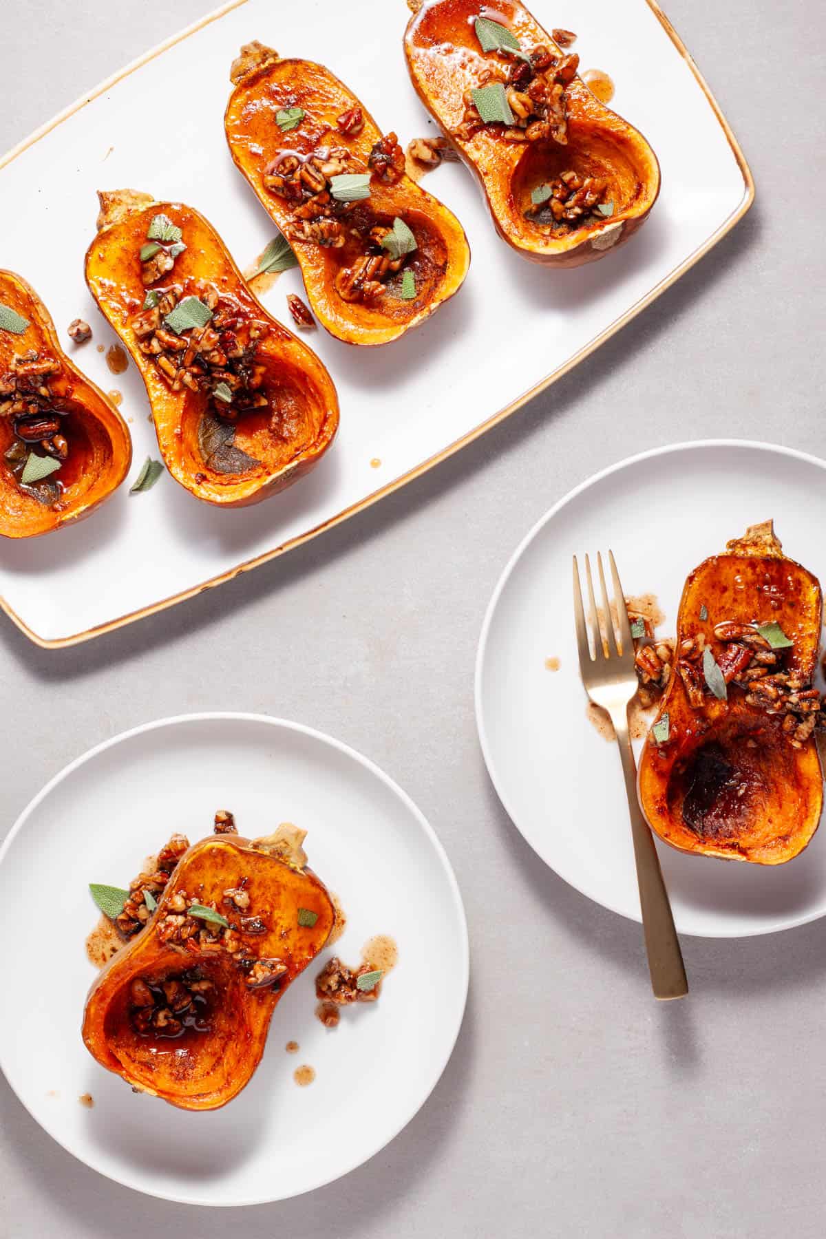 Roasted honeynut squash with maple pecans on a serving platter with a couple portions on smaller plates.