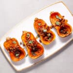 Roasted honeynut squash with maple pecans on a serving platter topped with fresh sage.