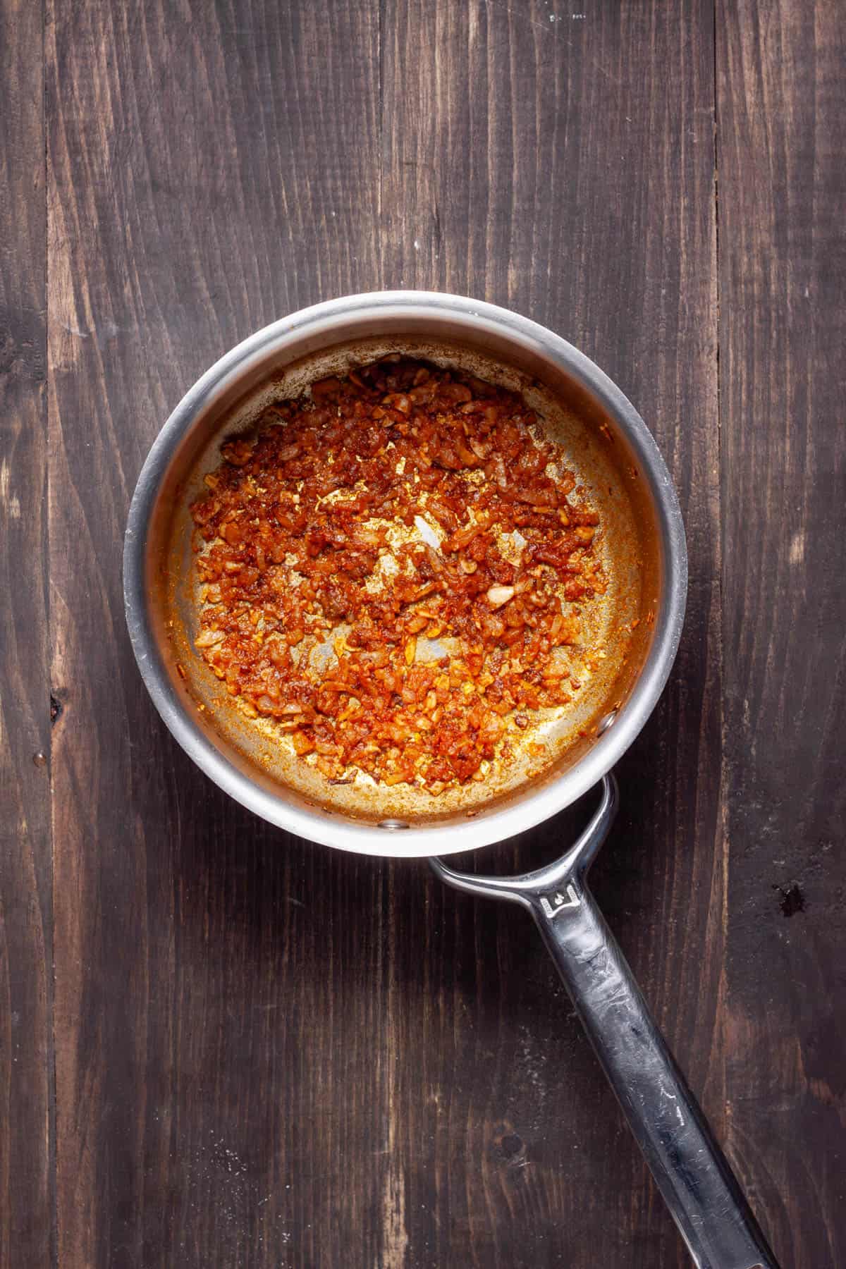 Minced onion and garlic cooking in a saucepan with cumin and paprika.