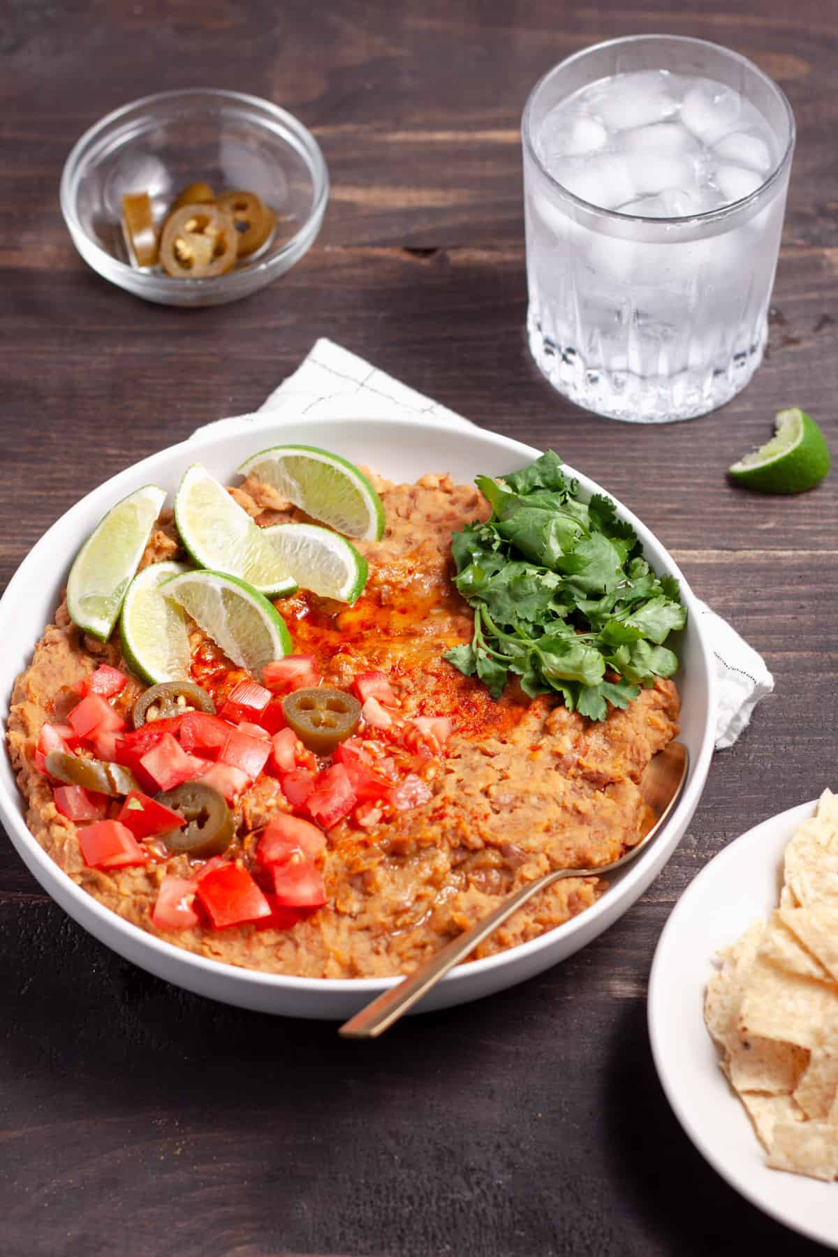 A bowl of vegan refried beans topped with cilantro, tomatoes, limes and pickled jalapenos.