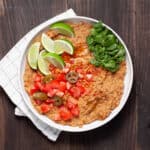 A bowl of vegan refried beans topped with cilantro, tomatoes, limes and pickled jalapenos.