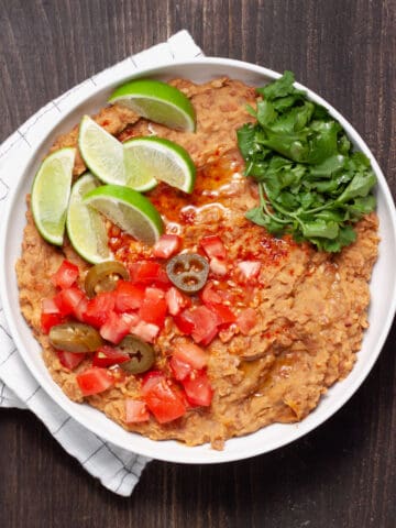 A bowl of vegan refried beans topped with cilantro, tomatoes, limes and pickled jalapenos.