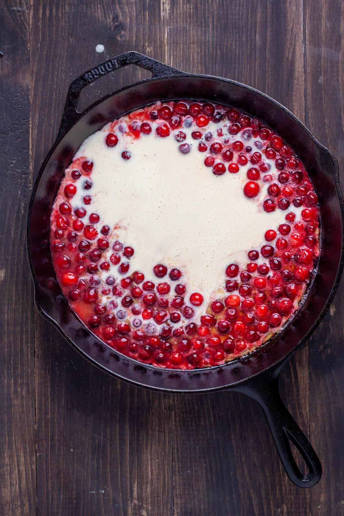 Dutch baby batter added to a large cast iron skillet with cranberries and butter in it.