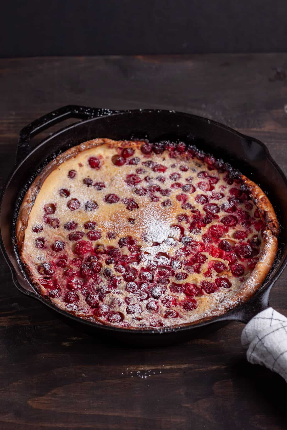 A cranberry dutch baby in a cast iron skillet dusted with powdered sugar.