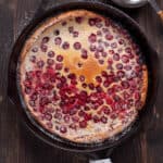 A cranberry dutch baby in a cast iron skillet dusted with powdered sugar.
