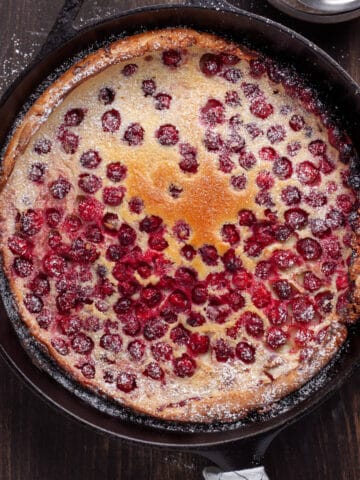 A cranberry dutch baby in a cast iron skillet dusted with powdered sugar.