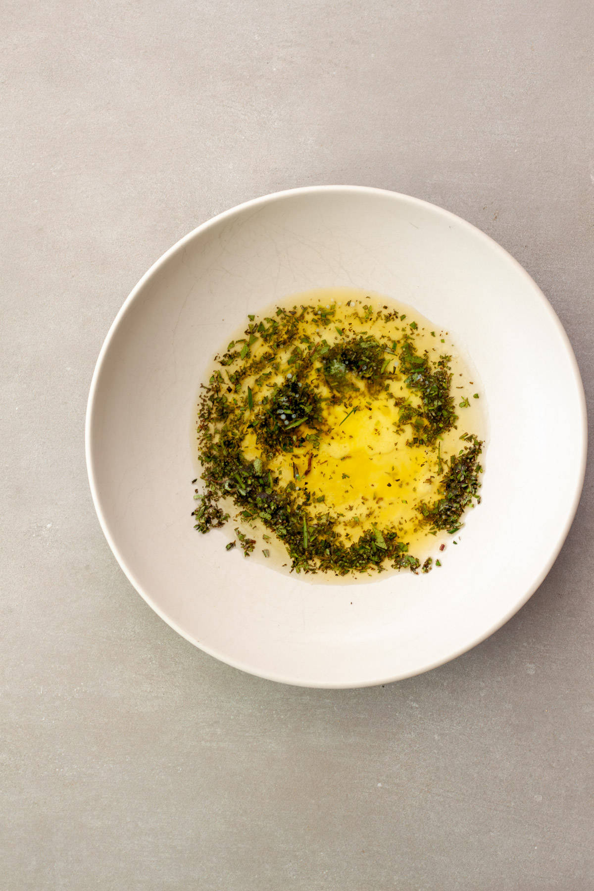 Melted butter, oil and fresh chopped herbs in a white mixing bowl.