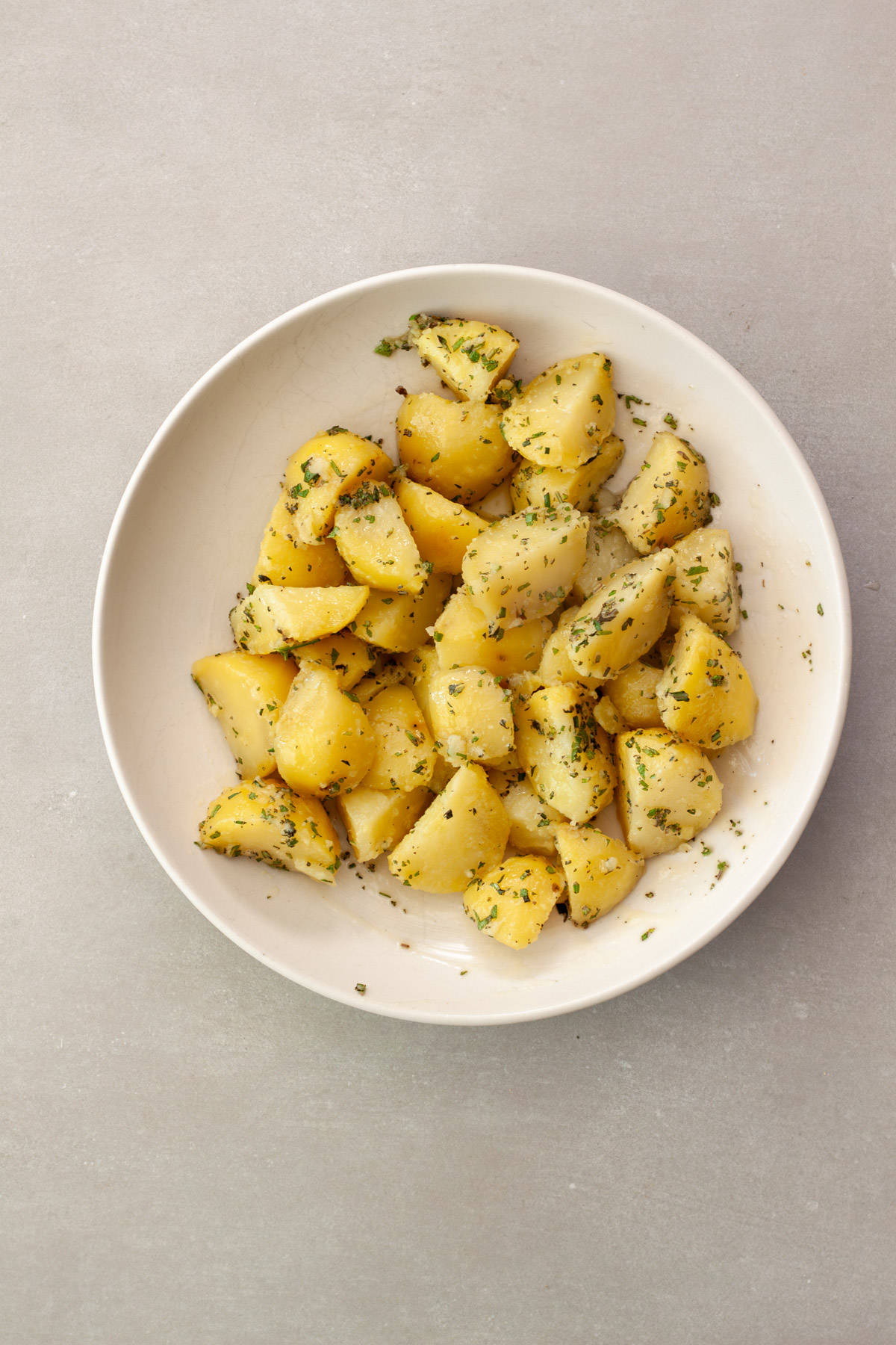 Partially cooked potatoes in a bowl with butter, oil and fresh herbs.