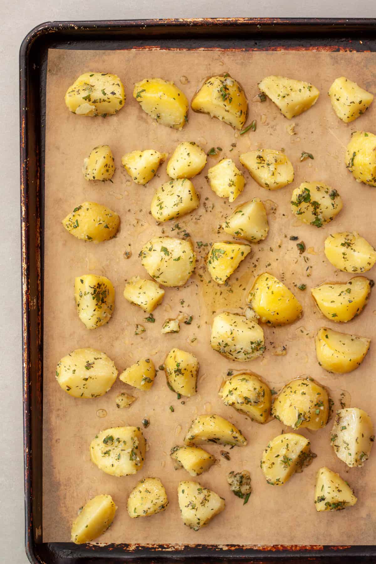 Potatoes tossed with butter and fresh herbs on a parchment lined baking sheet getting ready to be roasted.