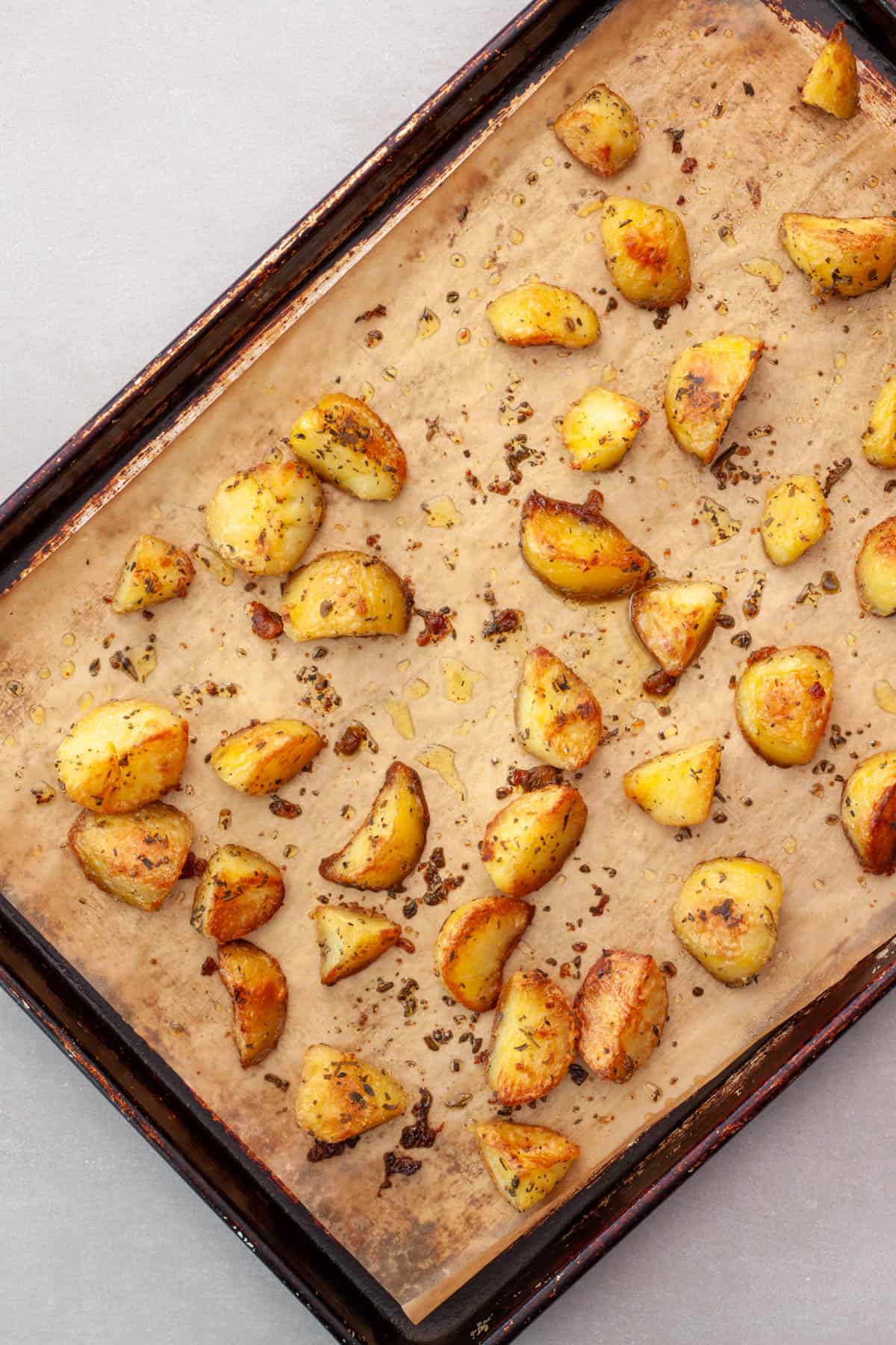 Freshly roasted herb potatoes on a parchment lined baking sheet.