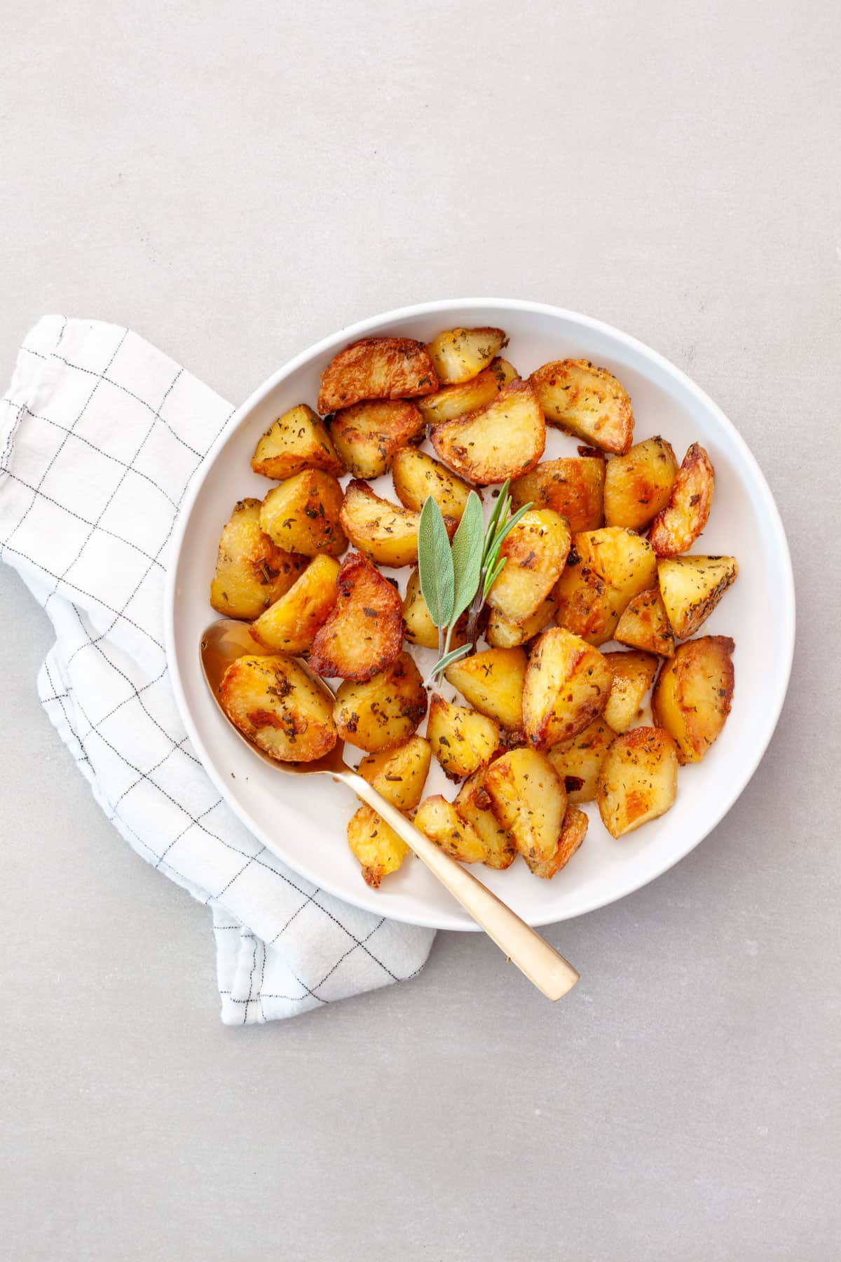 Crispy herb roasted potatoes in a serving bowl topped with fresh herbs.