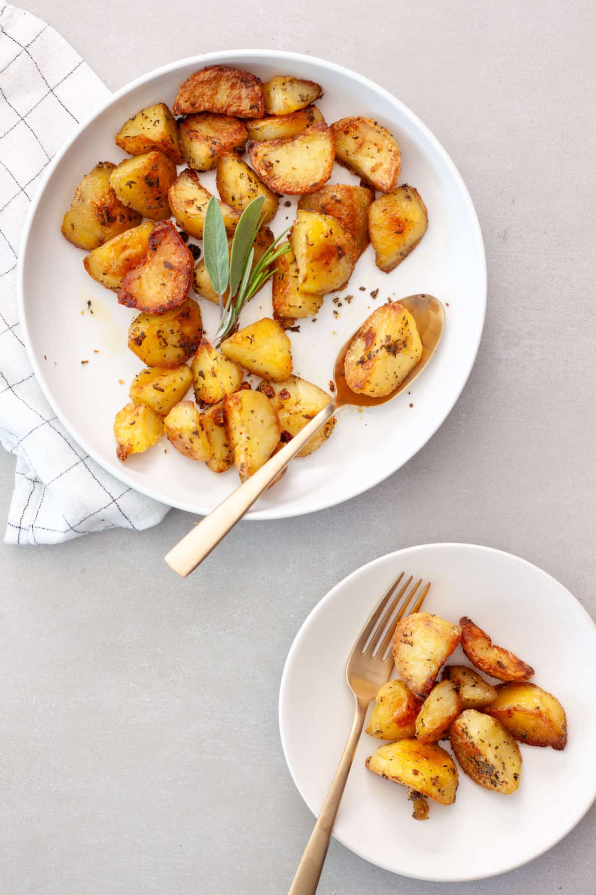 Crispy herb roasted potatoes in a large bowl getting serving to a small plate.